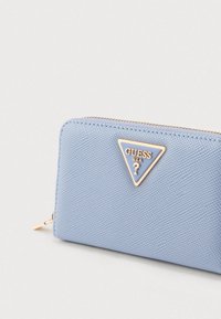 Világoskék texturált pénztárca aranyszínű háromszög alakú logó díszítéssel. Cipzáras záródással és sima élekkel rendelkezik. Kompakt, téglalap alakú forma.