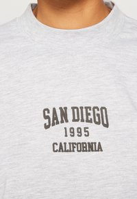 Sudadera de algodón gris con un cuello redondeado, que presenta un texto oscuro: "SAN DIEGO 1995 CALIFORNIA". Textura suave, diseño casual.