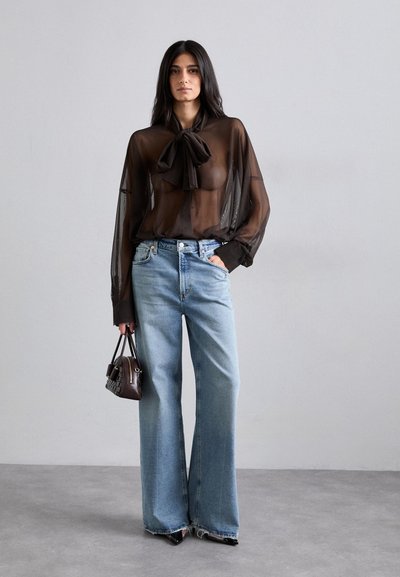 Durchsichtige schwarze Bluse mit Schleifen-Detail, kombiniert mit hellblauen weitem Jeans und einer kleinen braunen Handtasche. Texturierte Materialien, lässiger Stil.