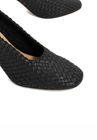 Black woven leather heels with a rounded toe and smooth texture. Features a low-cut vamp and a subtle sheen on the surface.