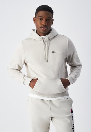 Sudadera ligera gris claro con cordones, bolsillo tipo canguro y logotipo de Champion bordado en rojo y azul. Tejido suave y liso, ajuste holgado.