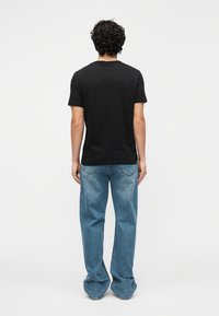 Svart t-skjorte med korte ermer, brukt sammen med lyseblå vide bukser, med en klassisk passform og enkel design, sett bakfra.