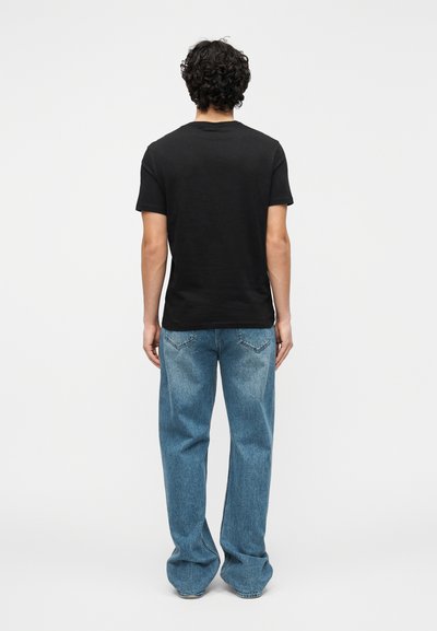 T-shirt noir à manches courtes porté avec un jean large bleu clair, présentant une coupe classique et un design simple, vu de dos.