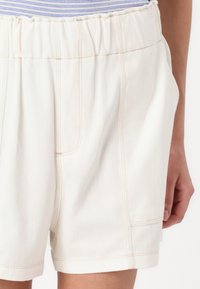Shorts blancs avec une texture herringbone subtile, une taille élastique et des coutures contrastées. Comprend des poches latérales et une coupe décontractée.