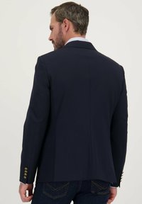 Marineblazer met een gestructureerd ontwerp, enkele split aan de achterkant, en goudkleurige knopen op de mouwen. De stof oogt glad en op maat gemaakt.