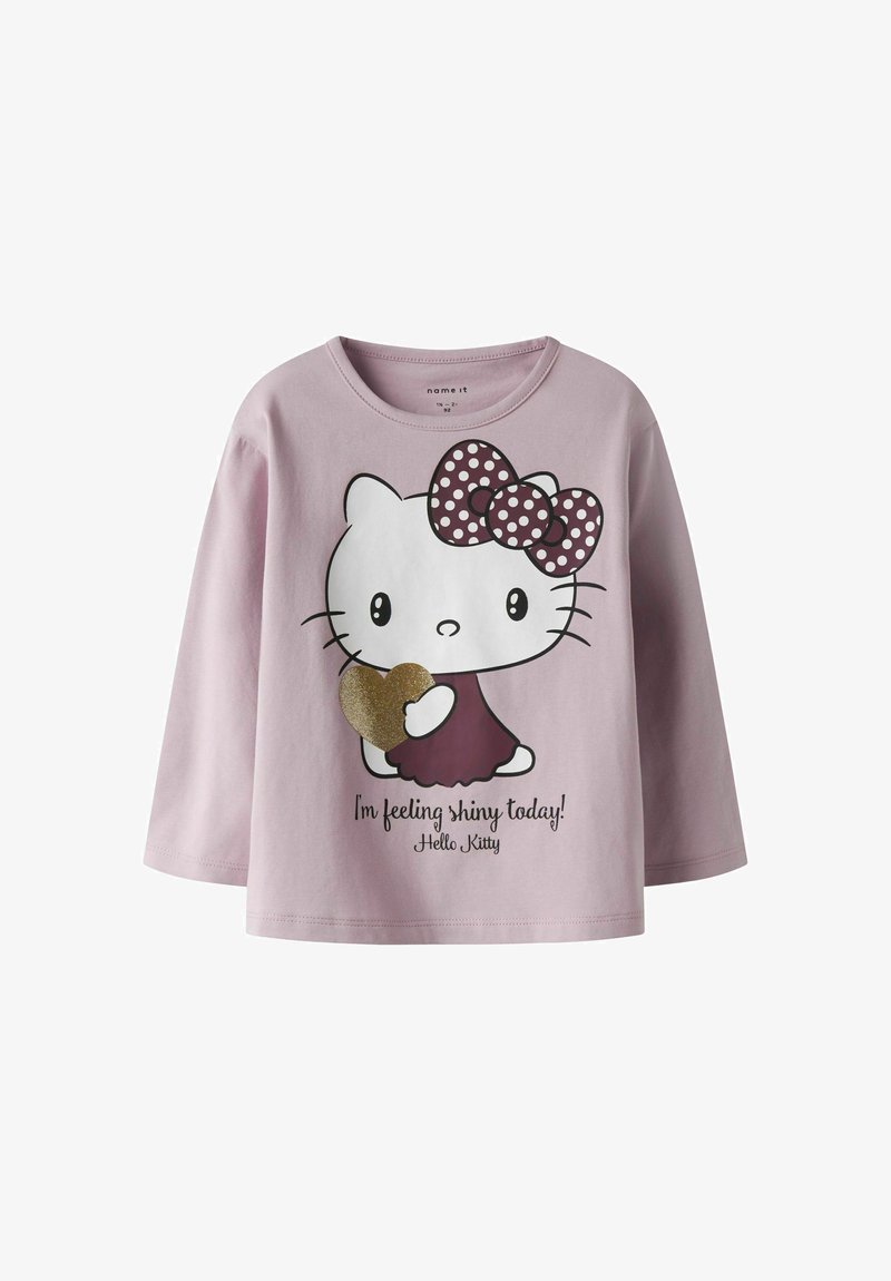 Jasnoróżowa koszulka z długim rękawem z grafiką Hello Kitty, z kokardą w kropki i błyszczącym sercem, towarzyszy tekst.