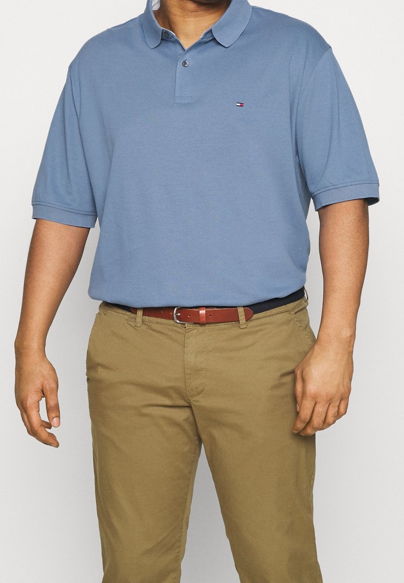 Ljusblå polo med kort ärm, liten logotyp på bröstet, kombinerad med beige chinos och ett brunt bälte, med en slät textur.