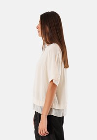 Top corto a maniche corte beige chiaro con un design a strati, caratterizzato da una texture liscia e una leggera lucentezza, ideale per outfit casual.