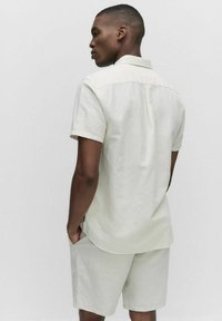 Lichtbeige kortebloem shirt met een kraag, gestructureerde stof en achterplooidetail, gecombineerd met bijpassende lichte shorts.