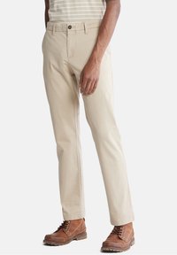 Beige bomullsbyxor med rak benform, med knappstängning och sidofickor, tillsammans med bruna snörstövlar.