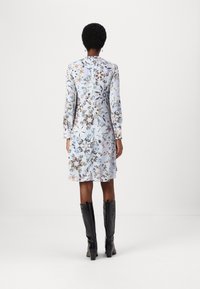 Vestido floral azul claro con mangas largas, que presenta una espalda abotonada. Combinado con botas negras hasta la rodilla. Tejido suave, con un patrón floral detallado.