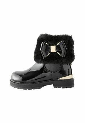 Bottines noires en vernis avec un col en fausse fourrure, un grand nœud décoratif et un accent doré sur le talon. Semelle en caoutchouc texturé pour une meilleure adhérence.