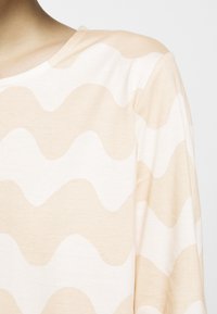 Tissu à rayures ondulées beige et blanc sur une chemise à manches longues, montrant l'épaule et la partie supérieure de la poitrine d'une personne.