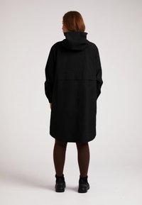 Zwarte waterdichte lange jas met een capuchon, met een relaxte pasvorm en een achterste vent voor ventilatie. Gecombineerd met donkere leggings en schoeisel.