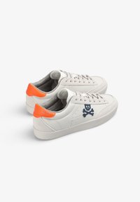 Weiße Leder-Sneaker mit orangen Fersenakzenten, grauem Innenmaterial und blauem Totenkopfdesign an der Seite. Sie verfügen über flache Schnürsenkel und eine strukturierte Oberfläche.