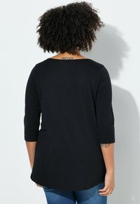 Haut noir, ample, à manches trois-quarts et à large encolure. Le tissu semble doux avec une texture lisse.