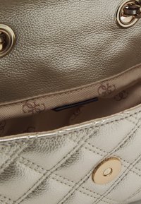 Metalowa złota skórzana torebka o pikowanym wzorze. Posiada gładką podszewkę z subtelnym wzorem logo oraz bezpieczne zapięcie na zatrzask.