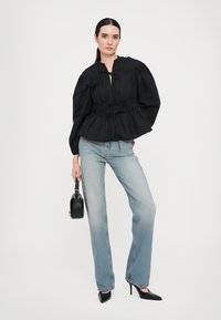 Svart bluse med puffermer og elastisk midje, kombinert med lyseblå rette jeans. Svart spisshæl og en liten svart håndveske.