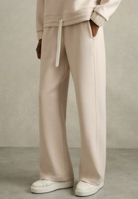 Hellbeige weite Sweatpants aus weichem Stoff, mit einem Drawstring-Bund und seitlichen Taschen, kombiniert mit weißen Sneakers.