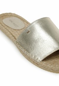 Slip-on sandal med metallic guld læderrem og vævet jutesål, der har et lille gravert logo på remmen.