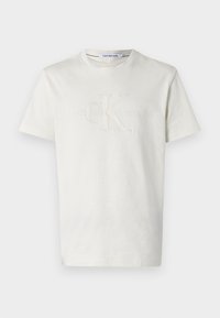 Krémové bavlněné tričko s kulatým výstřihem, na kterém je vyražené logo 'CK' a text 'Calvin Klein Jeans' pod ním.