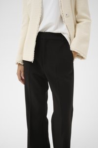 Elfenbeinfarbener, strukturierter Blazer mit ausgefransten Kanten und Knopfverschluss, kombiniert mit schwarzen, maßgeschneiderten Hosen mit Seitentaschen und geradem Bein.