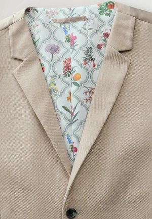 Beige textured blazer with notched lapels and a black button, showcasing a colorful floral-patterned lining.