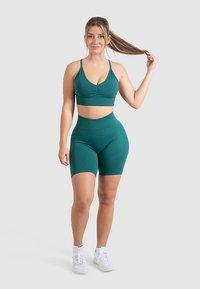 Vidren urheilu rintaliivit ja shortsit joustavasta kankaasta. Rintaliiveissä on poimutettu etuosa, ja shortseissa on korkea vyötärö ja sileä pinta.