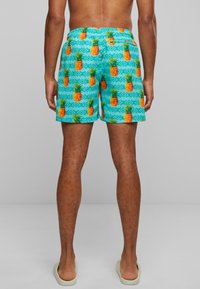 Shorts de bain bleu clair avec un imprimé ananas orange vif et un motif géométrique. Taille élastique et coupe décontractée.