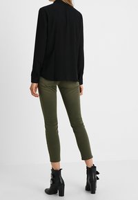 Svart långärmad tröja i kombination med olivgröna skinny jeans och svarta anklarstövlar med remmar och klack.