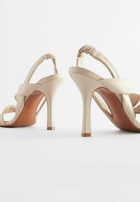 Beige Absatzsandalen mit einer weichen Lederoberfläche, die über Kreuz geschnallte Riemen und einen gerafften Knöchelriemen verfügen. Schlanke, konisch zulaufende Absätze.
