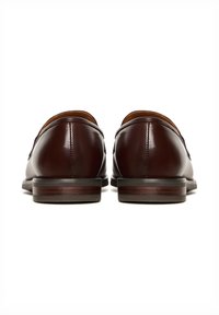 Paar polierte dunkelbraune Lederschuhe, von hinten gezeigt, mit niedrigen gestapelten Absätzen auf weißem Hintergrund.