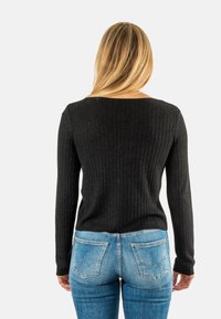 Maglione nero a costine con maniche lunghe, scolla a barca e finitura testurizzata. Abbinato a jeans aderenti blu chiaro con tasche posteriori classiche.