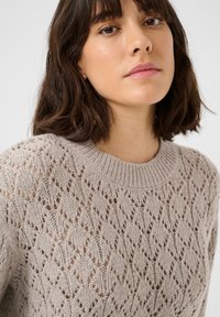 Maglione a maglia beige chiaro con motivo a rombi, scollatura rotonda e una texture che conferisce un aspetto delicato e leggero.