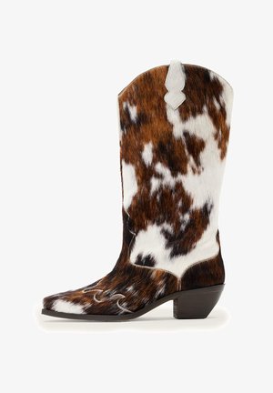 Cowhide-patterned mid-calf western boot with pointed toe, decorative stitching, pull tab, and low stacked heel in brown, white, and black tones.