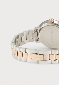 Montre en acier inoxydable avec un bracelet bicolore comportant des maillons argentés et en or rose. Boîtier rond avec un accent en cristal sur la couronne.