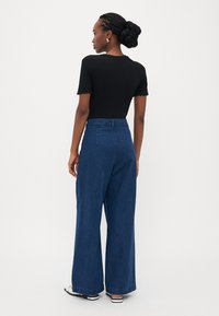 Black ribbed t-shirt with scalloped sleeves, paired with high-waisted, wide-leg blue denim jeans. Back view shows relaxed fit and visible waistband.