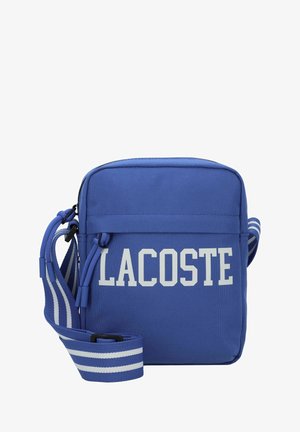 Niebieska prostokątna torba na ramię z białym napisem „LACOSTE” oraz regulowanym, niebieskim paskiem z białymi poziomymi paskami.
