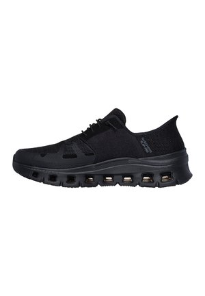 Zapatilla deportiva negra con parte superior tejida transpirable, cierre de cordones y suela gruesa acolchada con múltiples aberturas de ventilación.