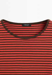 Zbliżenie na czerwoną i brązową poziomo prążkowaną koszulę z okrągłym dekoltem i metką Massimo Dutti wszytą od środka.