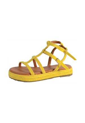 Sandalia plana amarilla con tiras trenzadas, hebilla ajustable en el tobillo, plantilla acolchada marrón y suela texturizada.