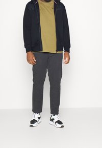 Black zip-up hoodie, olive green t-shirt, gray tapered pants, and black and white athletic shoes. Simple, casual outfit with no patterns.