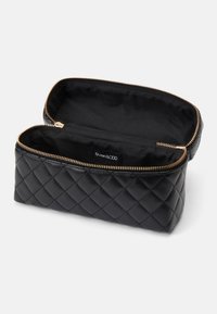 Svart quiltet kosmetikkbag med gullglidelås, med en glatt skinnutside og et svart stoffinteriør. Åpen for synlighet.