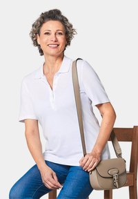 Witte polo met korte mouwen, voorzien van een kraag en knopen, gecombineerd met blauwe jeans en een beige schoudertas.