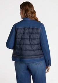 Chaqueta de abrigo de mezclilla y color marino con un respaldo acolchado, cuello estrecho y detalles de costura. Corte ajustado con mangas largas.