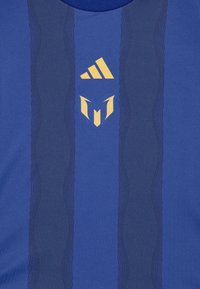 Sininen urheilupaita, jossa on teksturoitu suunnittelu, ja kultaiset yksityiskohdat Adidaksen logossa sekä keskellä oleva emblem.