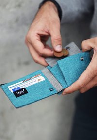 Teal fabric wallet with gray lining, features card slots, a coin pocket, and an RFID symbol. Wallet is open, held by a hand.