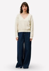 Pull col en V crème avec un tricot texturé, associé à un pantalon large en velours côtelé bleu foncé, doté d'un tissu doux à côtes et de larges revers.
