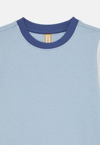 Lys blå kortermet skjorte med ribbet marineblå krage. Myk tekstur, enkelt design, og har en gul etikett inni nakken.