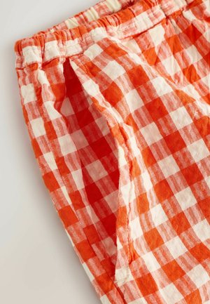 Kraťasy z červené a bílé kostkované látky s elastickým pasem, vyrobené z texturované bavlněné tkaniny a s volným střihem.
